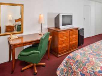 Mirror, desk with chair, telephone and lamp, wooden drawer unit with tv, fridge, carpet flooring