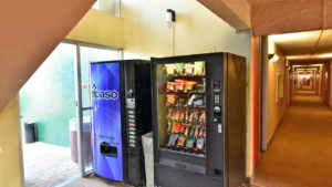 Snack and soft drinks vending machines, doorway to the exterior and interior corridor with carpet flooring