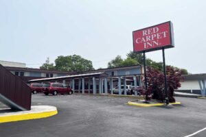 Brand signage, two story building with exterior guestroom entrances and covered walkways, parking spaces, small tree