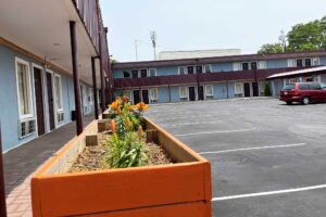 Two story building with exterior guestroom entrances and covered walkways, parking spaces, wooden flower boxes