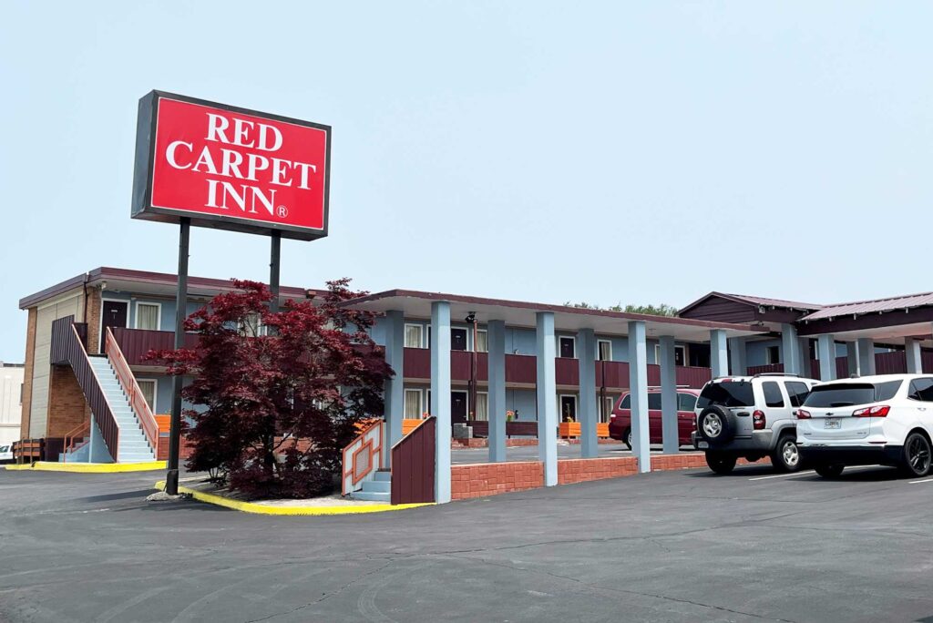 Brand signage, two story building with exterior guestroom entrances and covered walkways, parking spaces, small tree