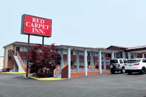 Brand signage, two story building with exterior guestroom entrances and covered walkways, parking spaces, small tree