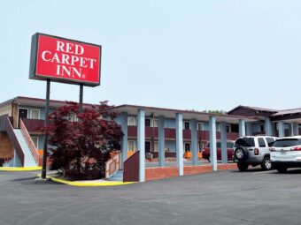 Brand signage, two story building with exterior guestroom entrances and covered walkways, parking spaces, small tree