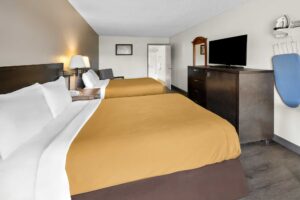 Two queen beds, night stand with telephone, wall bedside lamps, easy chair, doorway to bathroom, mirror, wooden unit with TV, ironing board and iron, laminate flooring