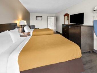 Two queen beds, night stand with telephone, wall bedside lamps, easy chair, doorway to bathroom, mirror, wooden unit with TV, ironing board and iron, laminate flooring