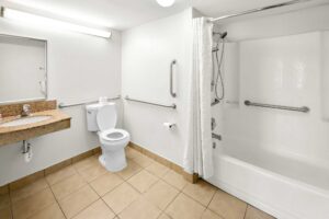 Vanity unit, mirror, toilet with grab handles, shower tub with grab handles and shower curtain, tiled flooring
