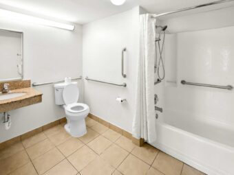 Vanity unit, mirror, toilet with grab handles, shower tub with grab handles and shower curtain, tiled flooring