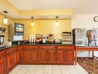 Breakfast display counter with cereal dispensers, coffee machine, juice machine, toaster, bakery display cabinet, fridge for chilled breakfast items, tiled and carpet flooring