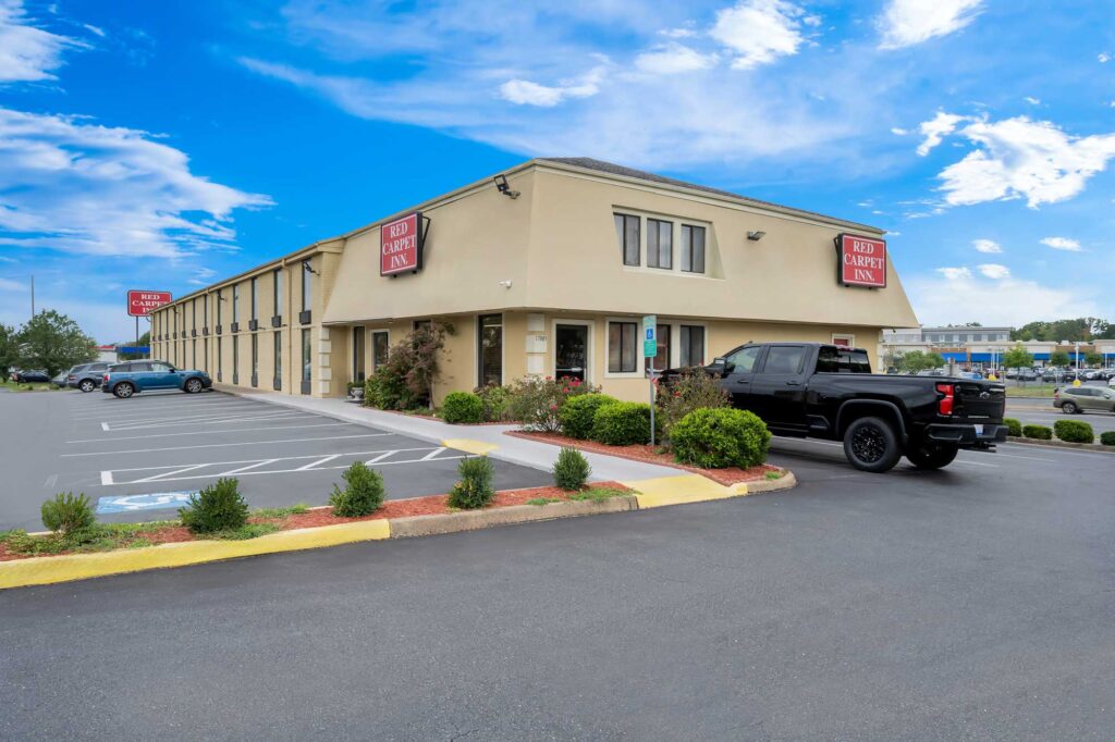 Two story building, hotel entrance, landscaping with flowering shrubs, small tree and shrubs, parking spaces