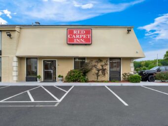 Hotel entrance, landscaping with small shrubs and tree, brand signage, parking spaces