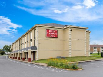 3 story building, landscaping with flowering shrubs and grassy areas, parking spaces