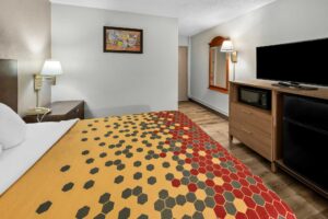 king bed, night stand with telephone, wall bedside lamp, art image, mirror, wall light, wooden unit with microwave, TV and fridge, laminate flooring