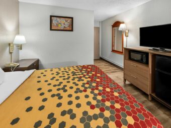 king bed, night stand with telephone, wall bedside lamp, art image, mirror, wall light, wooden unit with microwave, TV and fridge, laminate flooring