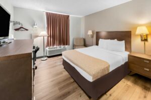 King bed, night stand, wall bedside lamps, easy chair, floor lamp, ironing board and iron, desk with chair, hanging rail and shelf with hangers, wooden unit with TV, laminate flooring