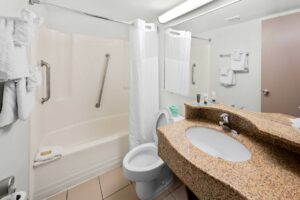 Shower tub with grab rails, bath mat and shower curtain, towel rail with towels, toilet, mirror, vanity unit, tiled flooring