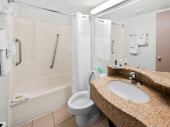 Shower tub with grab rails, bath mat and shower curtain, towel rail with towels, toilet, mirror, vanity unit, tiled flooring