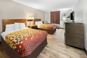Two queen beds, night stand, wall bedside lamps, easy chair, floor lamp, hanging rail with hangers, wooden unit with TV, laminate flooring