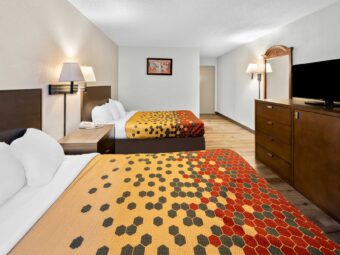 Two queen beds, night stand with telephone, wall bedside lamps, art image, wall light, mirror, wooden drawer unit with TV, laminate flooring