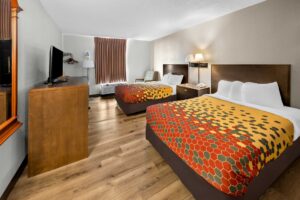 Two queen beds, night stand with telephone, wall bedside lamps, easy chair, floor lamp, hanging rail with hangers, wooden unit with TV, laminate flooring