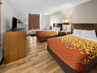 Two queen beds, night stand with telephone, wall bedside lamps, easy chair, floor lamp, hanging rail with hangers, wooden unit with TV, laminate flooring