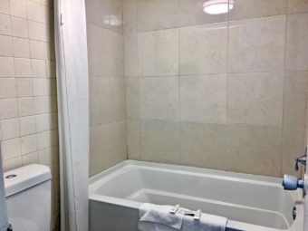 Shower tub, bathmat with amenities, shower curtain, tiled walls