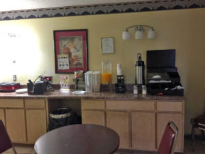 breakfast display counter, coffee pot, orange juice dispenser, cereal containers, waffle maker, tables and chairs