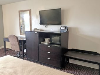 Desk, chair, wall mounted mirror, wooden unit with drawers, microwave, wall mounted flat screen tv, carpet flooring