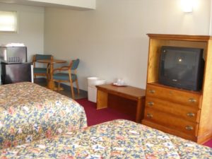 Two double beds, wooden console unit with drawers and tv, occasional tables, small table with chairs, fridge with microwave, carpet flooring