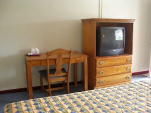 King bed, desk with chair, wooden tv console unit with drawers and tv, carpet flooring