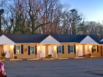 Exterior room entrances, parking spaces and trees behind the one story buildings