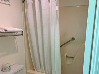 Shower tub with bath mat, bathroom amenities and shower curtain, wall mounted towel rail with folded towels