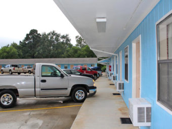 One story buildings, canopied walkway, exterior room entrances, paking spaces, large trees behind buildings