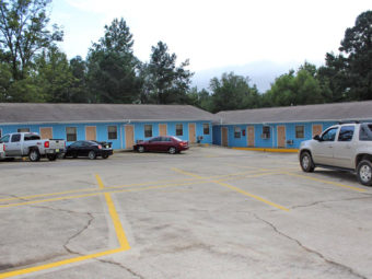 one story buildings with exterior room entrances, parking spaces, large trees behind buildings