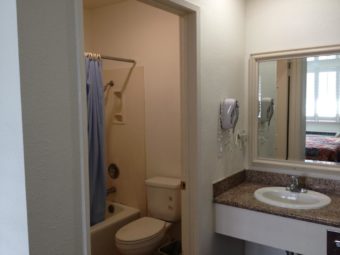 Vanity unit with sink, wall mounted mirror, dorway to bathroom, shower tub with shower curtain and toilet