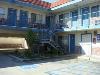 Two story building with exterior walkways and stairs, parking soaces on ground floor