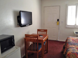 Small table with two chairs, wall mounted flat screen tv, fridge with microwave, queen bed, carpet flooring