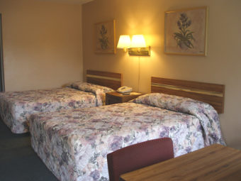 Two double beds, night stand with telephone, wall mounted bedside lights and art, small table and chair, carpet flooring