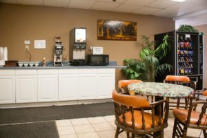 Breakfast counter display with coffee maker, juice dispenser, microwave, wall mounted art, potted plants, snack vending machine, table and chairs, tiled flooring