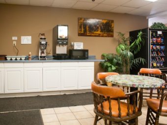 Breakfast counter display with coffee maker, juice dispenser, microwave, wall mounted art, potted plants, snack vending machine, table and chairs, tiled flooring