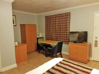 Queen bed, wooden drawer unit with flat screen tv, small table and chairs, wooden cupboard, fridge with microwave, laminte flooring