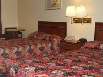 Two double beds, night stand with telephone and clock, wall mounted bedside lights and art, small table with chairs