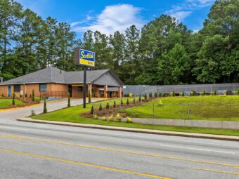 One story building with drive through entrance canopy, brand signage, landscaping with small trees, shrubs and grassy areas.