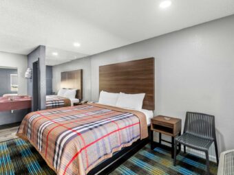 Chair, night stands with telephone, king bed, vanity unit, mirror, wall shelf with towels, mirrored wall, carpet and laminate flooring