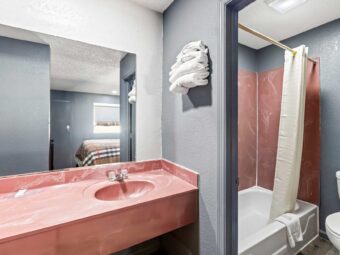 Vanity unit, mirror, wall shelf with towels, shower tub with shower curtain and bath mat, toilet, laminate flooring