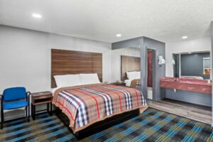 Chair, night stands with telephone, mirrored wall, vanity unit, mirror, wall shelf with towels, doorway to bathroom, carpet and laminate flooring