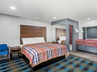 Chair, night stands with telephone, mirrored wall, vanity unit, mirror, wall shelf with towels, doorway to bathroom, carpet and laminate flooring