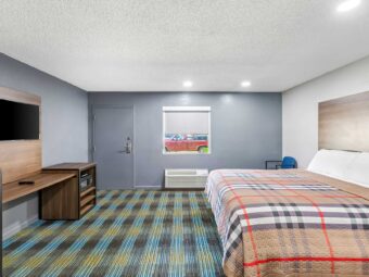 King bed, chair, wooden unit with microwave, TV and fridge, carpet flooring