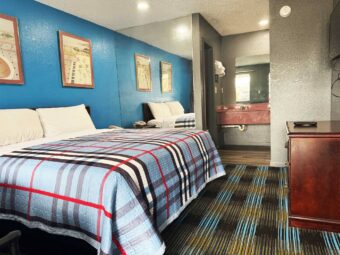 King bed, art images, mirrored wall, wooden drawer unit, wall mounted TV, vanity unit, rack with towels, mirror, carpet flooring