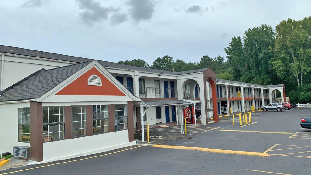 Two story building with exterior room entrances, parking spaces, overlooked by tall trees