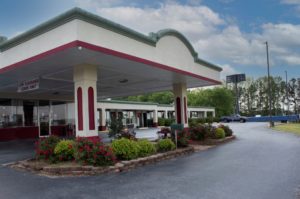 Hotel entrance with drive through canopy, landscaping with flowering shrubs, grassy areas and parking spaces